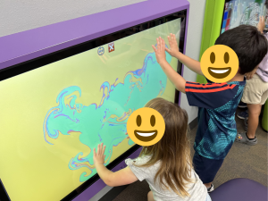 Children from Sunny Glen Children's Home explore an interactive touch screen display together during a fun dinosaur event, representing youth services in San Benito TX