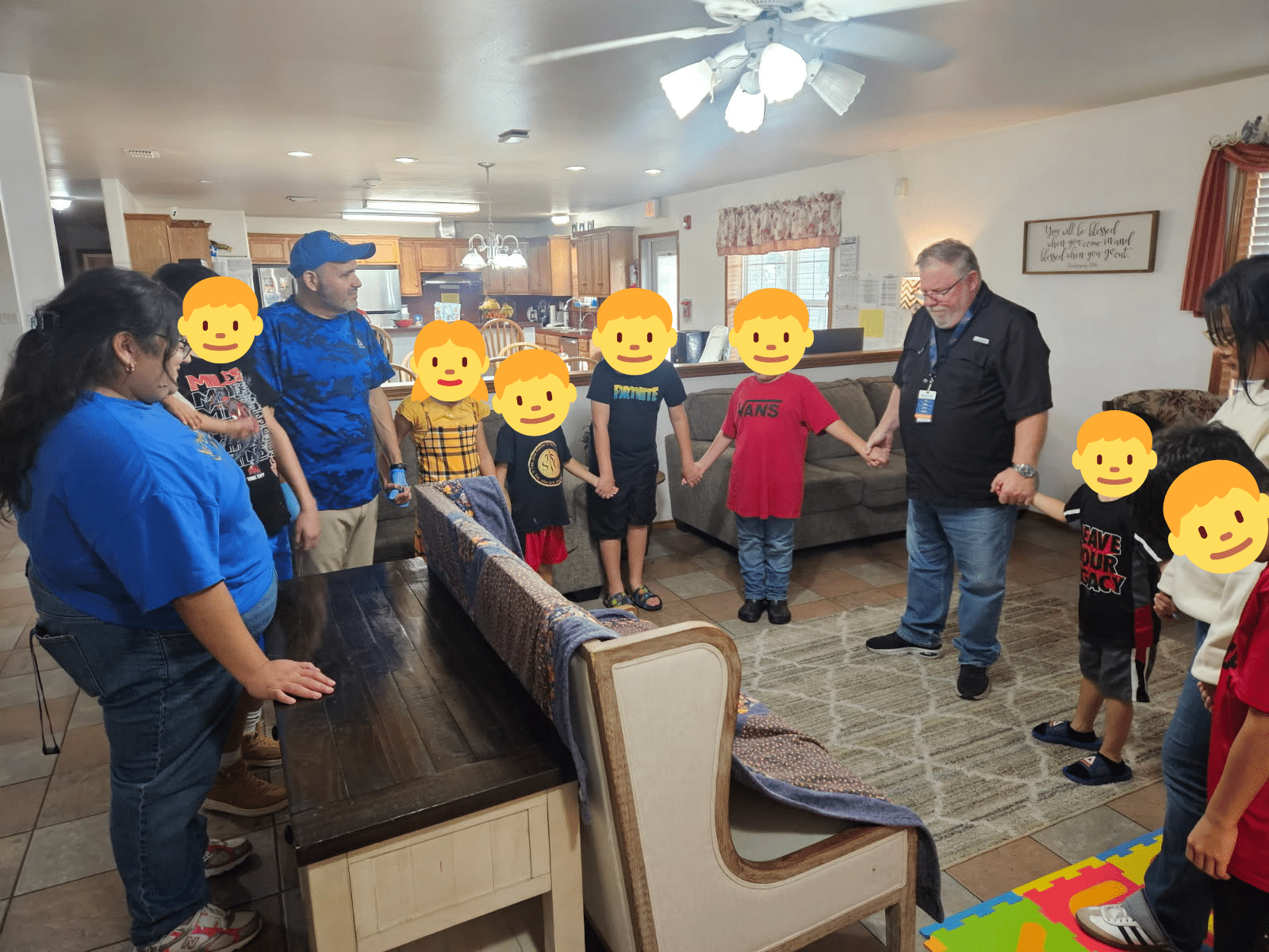Children and staff stand together holding hands in their cottage, sharing a moment of prayer before beginning a group activity, reflecting care, faith, and togetherness in daily life.