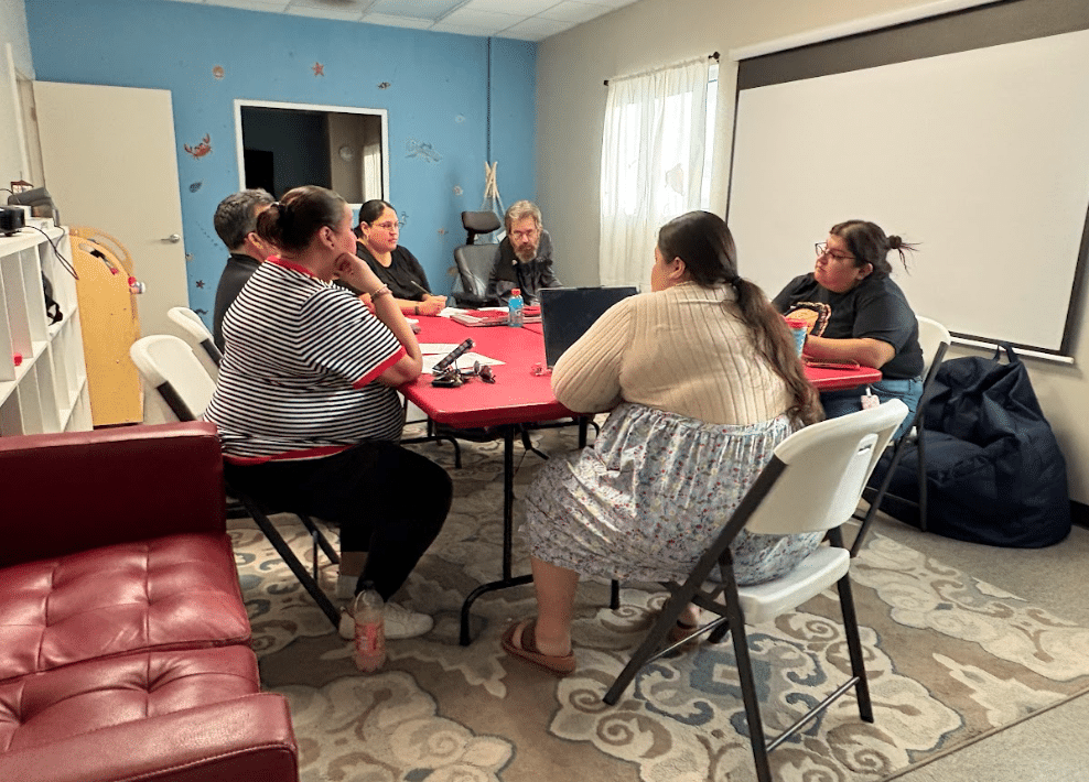 Sunny Glen staff gather around a table for a team meeting, discussing care plans and daily routines that support children through collaboration, training, and shared commitment.