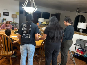 Children, staff, and Yellow House volunteers bow their heads in prayer at the dinner table, reflecting the daily care that recurring donations help sustain.