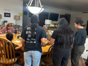 Children, staff, and Yellow House volunteers bow their heads in prayer at the dinner table, reflecting the daily care that recurring donations help sustain.